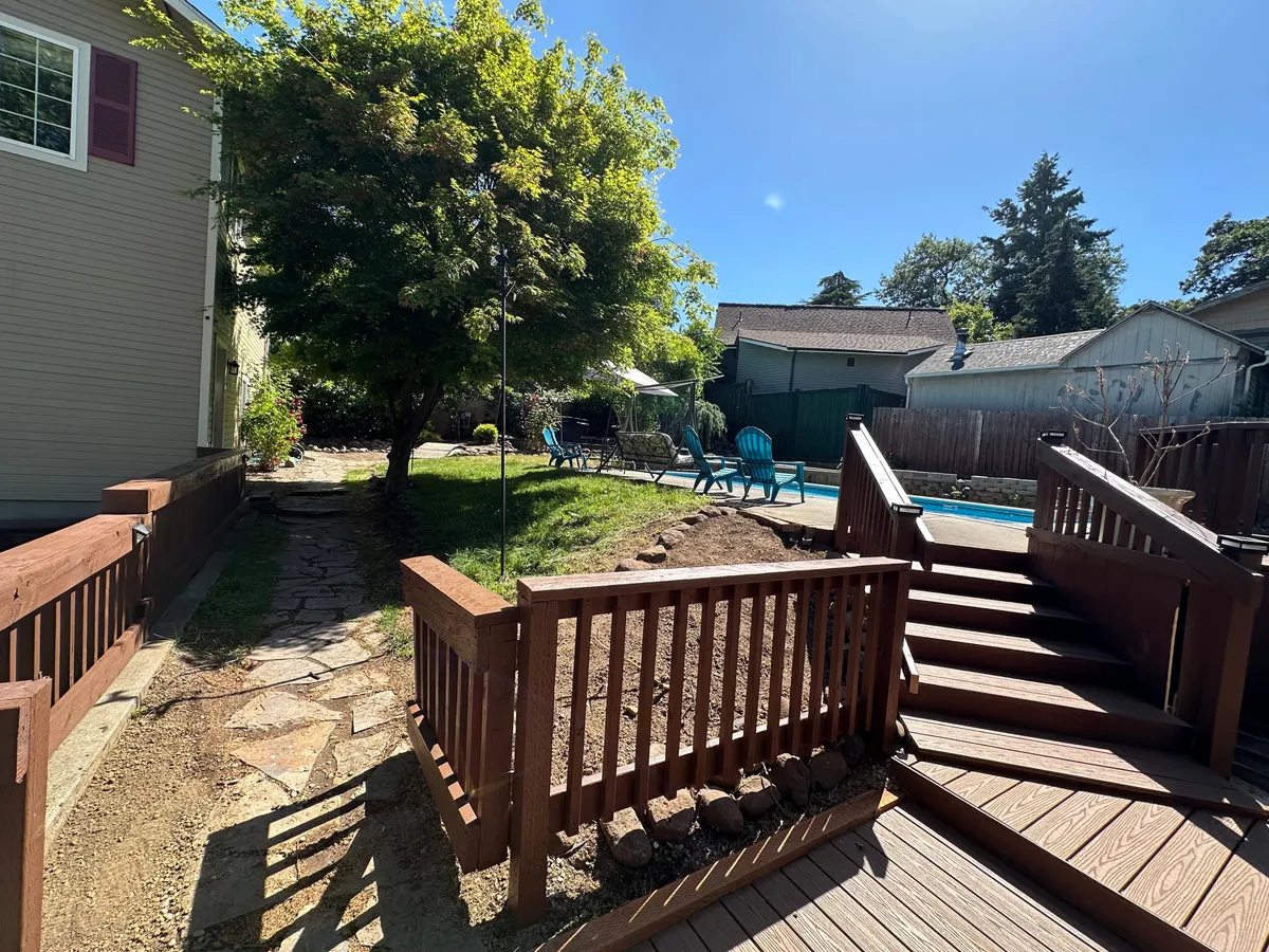 This exterior image features a sparkling swimming pool surrounded by a lush lawn, inviting deck, mature trees, and Adirondack chairs. The setting evokes a sense of relaxation and leisure, with ample space for sunbathing, morning coffee, or gathering with friends and family. The ambiance suggests a seamless connection between the property and its natural, vibrant surroundings.