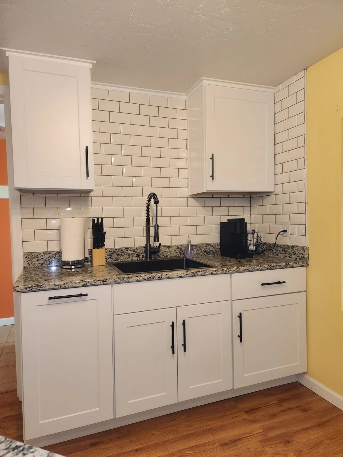 This image showcases a modern kitchenette featuring a granite countertop, sleek black faucet, white cabinetry, and a stylish subway tile backsplash. The clean and organized space is equipped for both meal preparation and social cooking, embodying a functional yet inviting environment.
