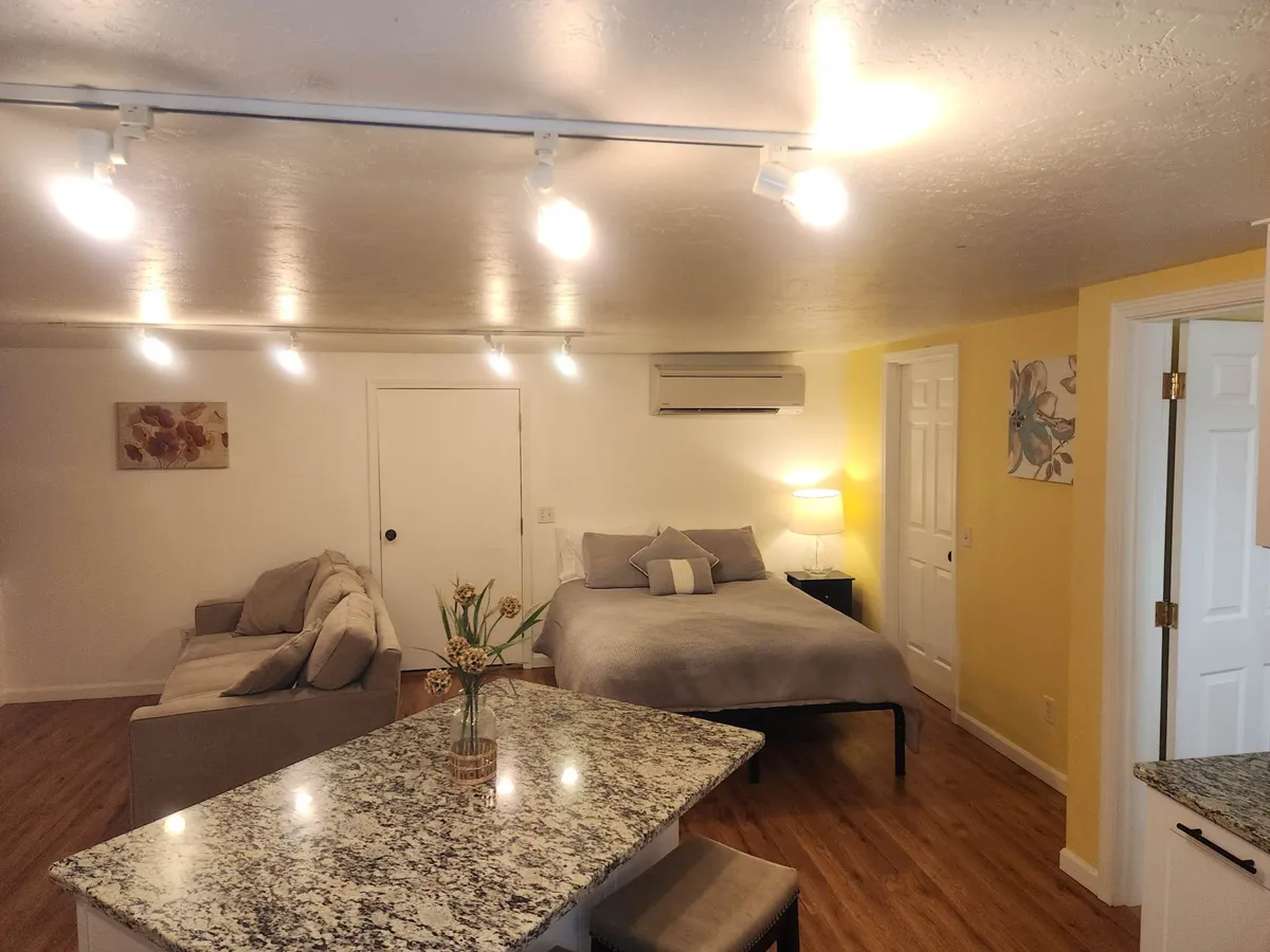 A warm, cozy scene of a living area with a plush sofa, bed, kitchen island, and a softly glowing lamp. The furnishings and layout foster an intimate, welcoming vibe—perfect for quiet conversations, laid-back mornings, or simply relaxing together.